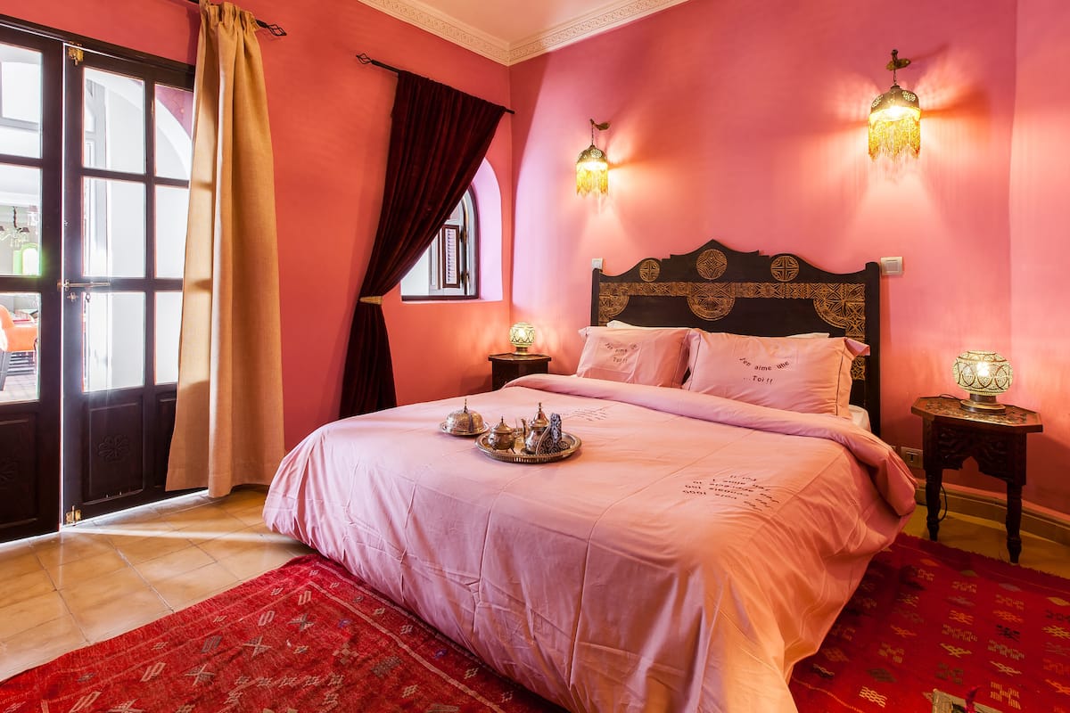 A room with a bed, a red carpet, a window with curtains, and wall-mounted lights.