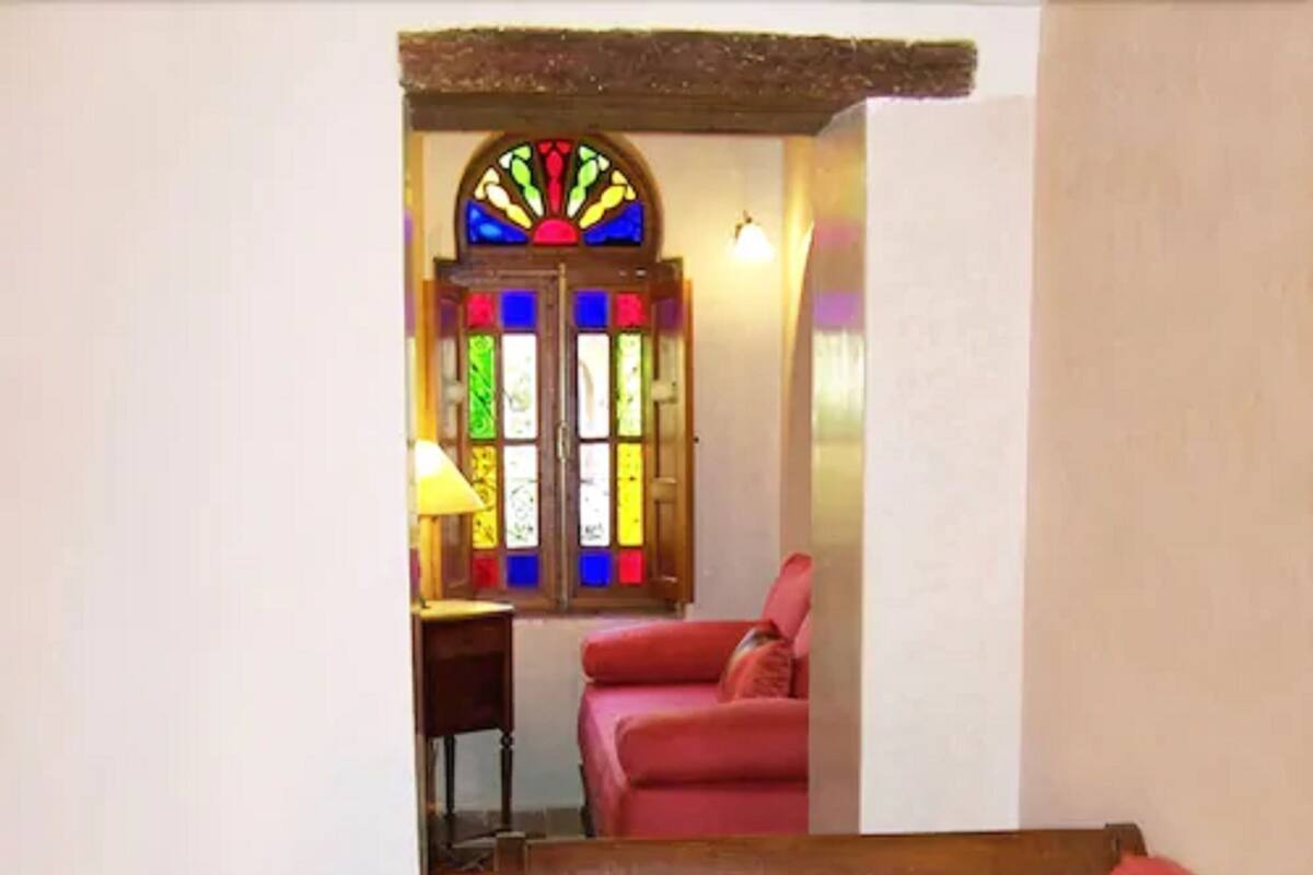 Ein Zimmer mit einer Holzbank, einem roten Stuhl und einem Buntglasfenster.