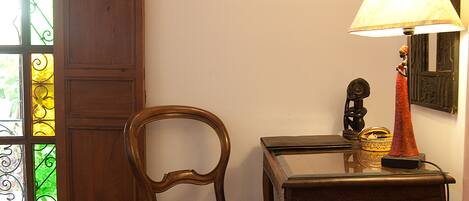 A room with a wooden chair, a table with a lamp, a framed picture on the wall, and a stained glass window.