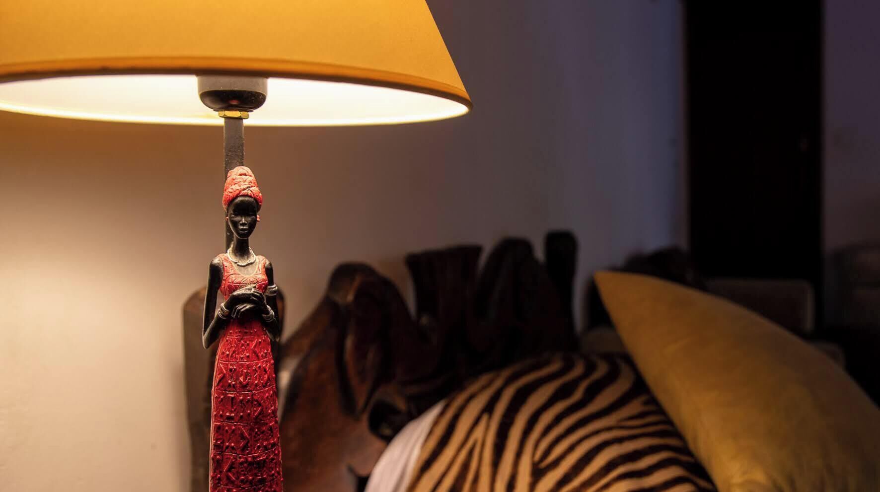 A lamp with a red tassel, a zebra-patterned pillow, and a yellow pillow on a bed.