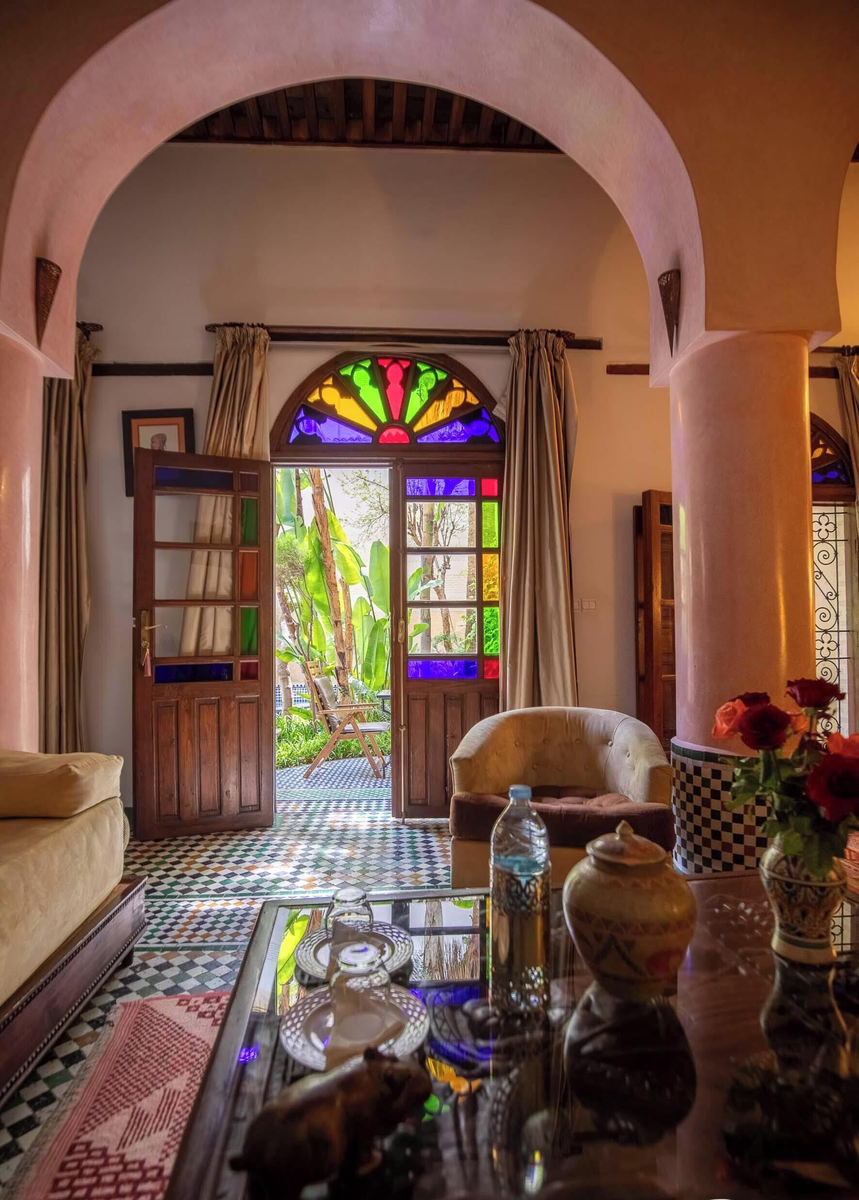 Una habitación con suelo a cuadros, un sofá, una mesa con objetos decorativos y vistas a través de una puerta con vidrieras.