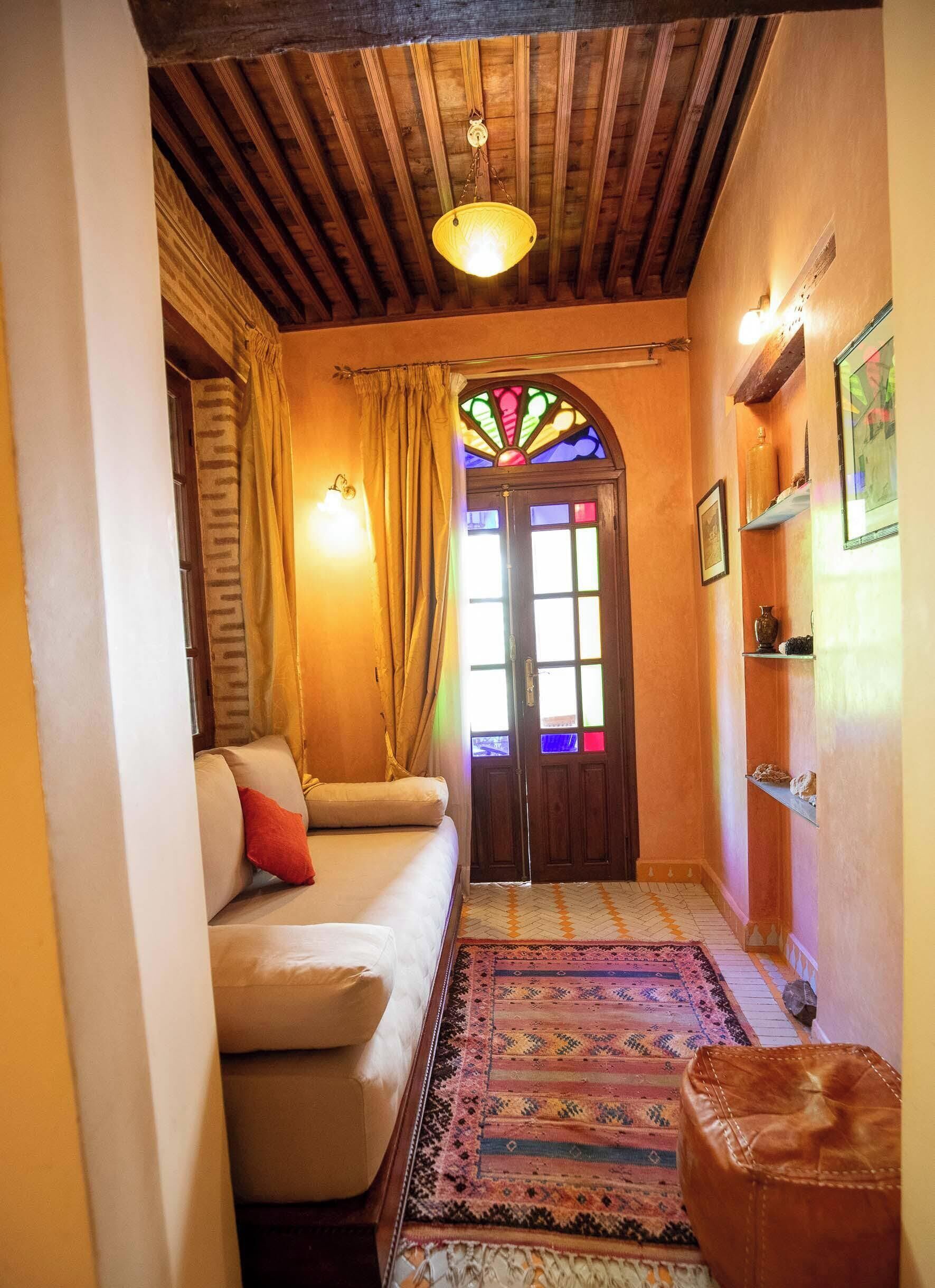 Una habitación acogedora con sofá, alfombra estampada, techo de madera y puerta de vitrales.