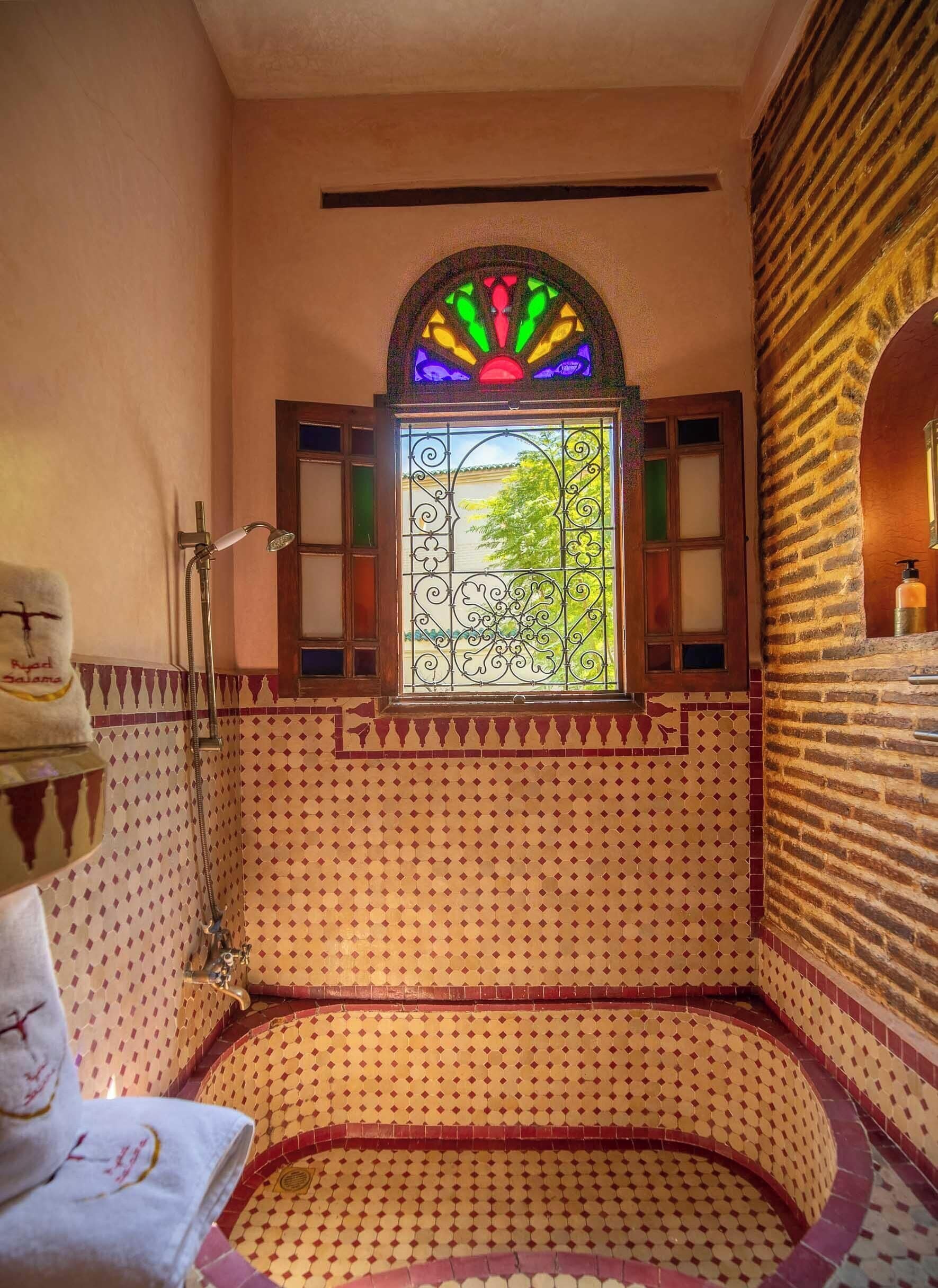 Une salle de bain avec une baignoire, une douche, une fenêtre ornée de vitraux et des murs à motifs.