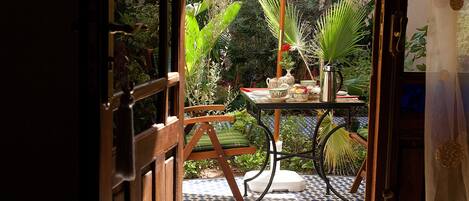 An open door to a room with a tiled floor, a wooden chair, a table with a vase, and various plants.