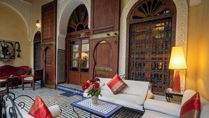 Un intérieur marocain traditionnel avec un canapé, une table basse ornée d’un vase de fleurs et des portes en bois richement décorées.