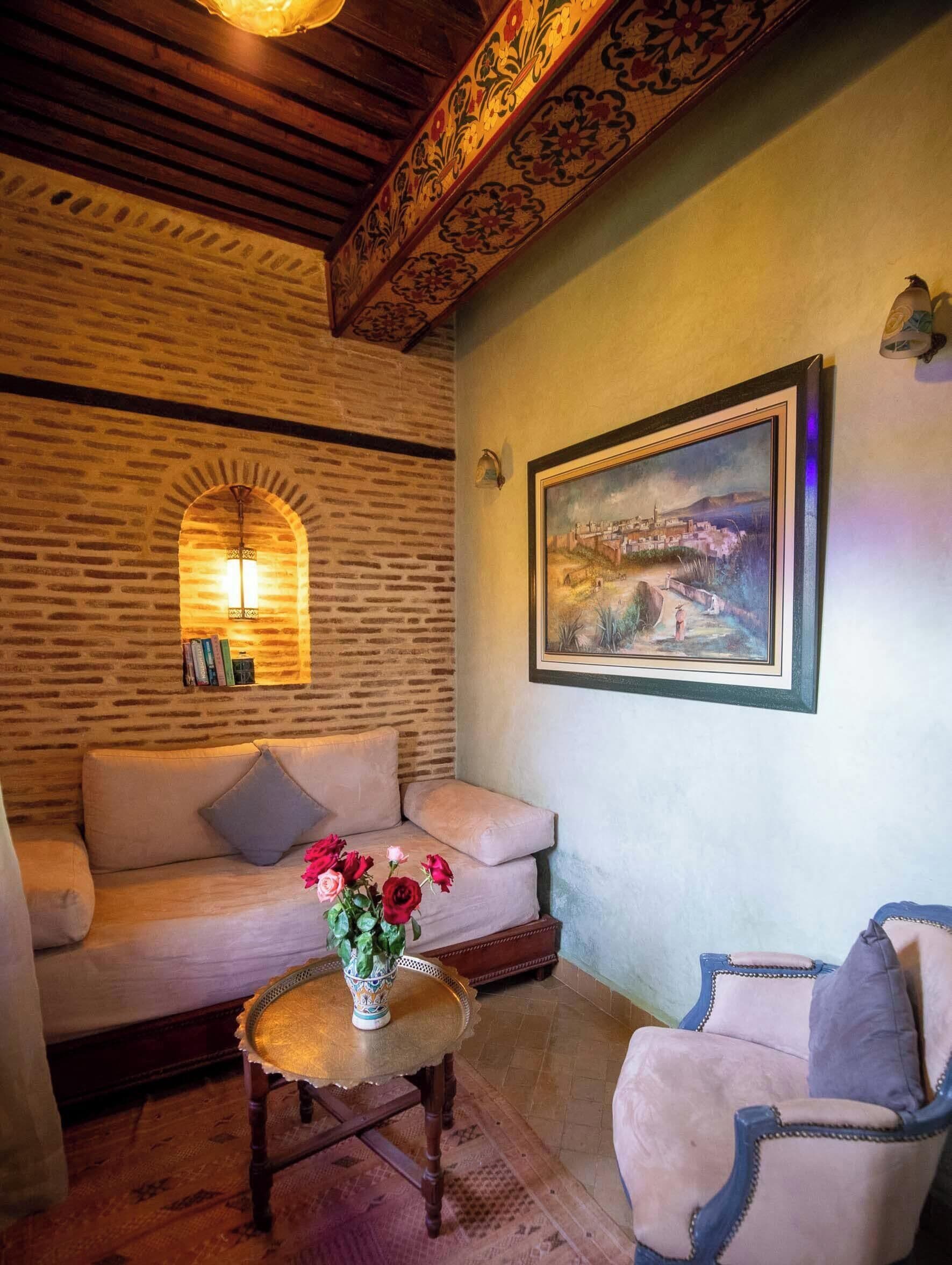 Una sala de estar acogedora con pared de ladrillo, un sofá, una mesa de centro con flores y un cuadro enmarcado.