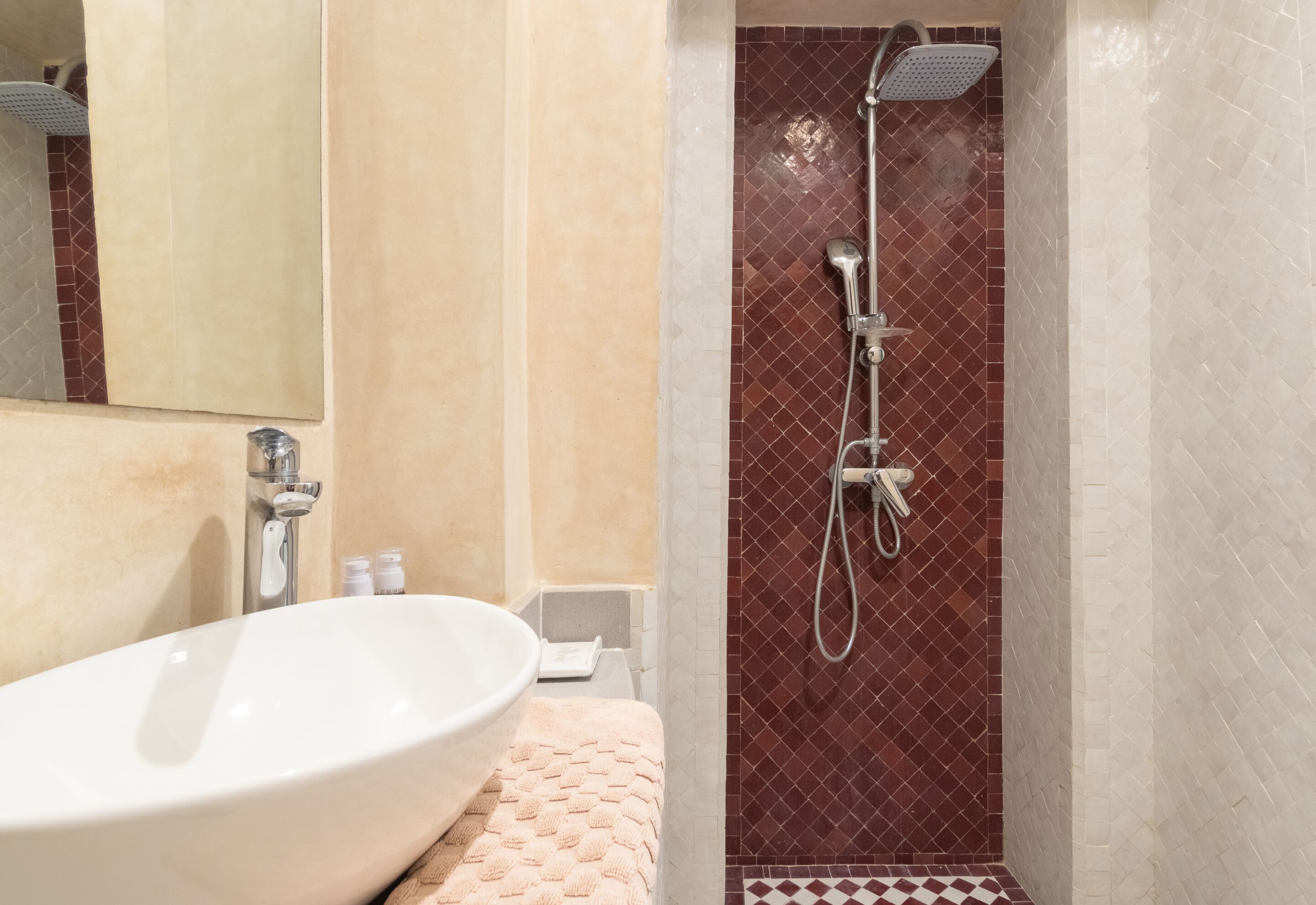 Een badkamer met een wit wastafelmeubel, een handdouche en een betegelde douchecabine.