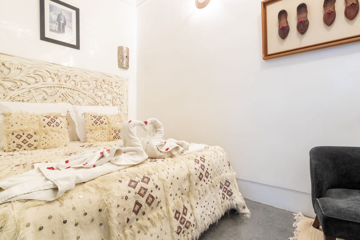 Een net opgemaakt bed met beddengoed met een patroon, een ingelijste foto aan de muur en een stoel in de hoek.