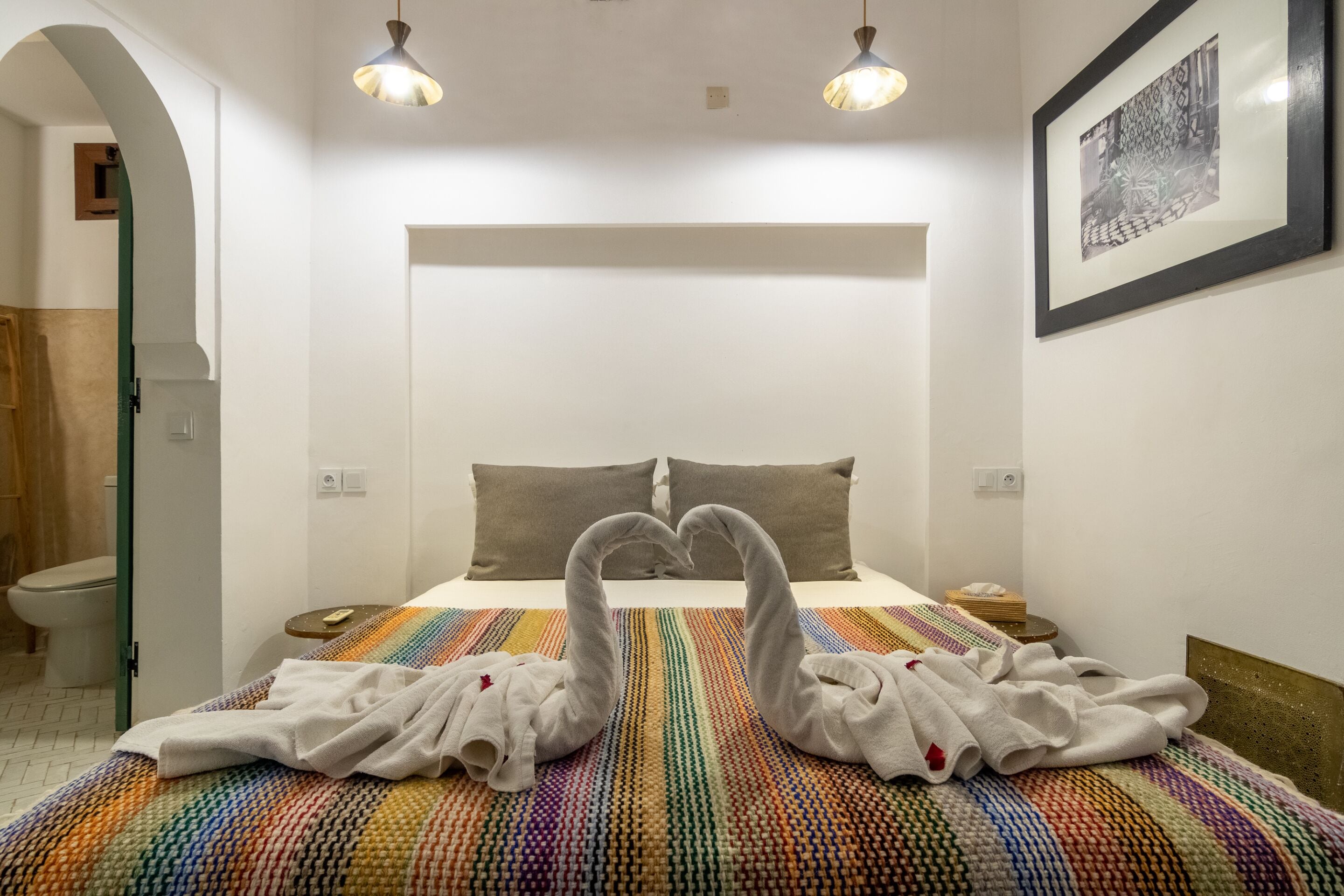 Habitación de hotel con cama, dos almohadas, mesita de noche, un cuadro enmarco y una composición artística con toallas.