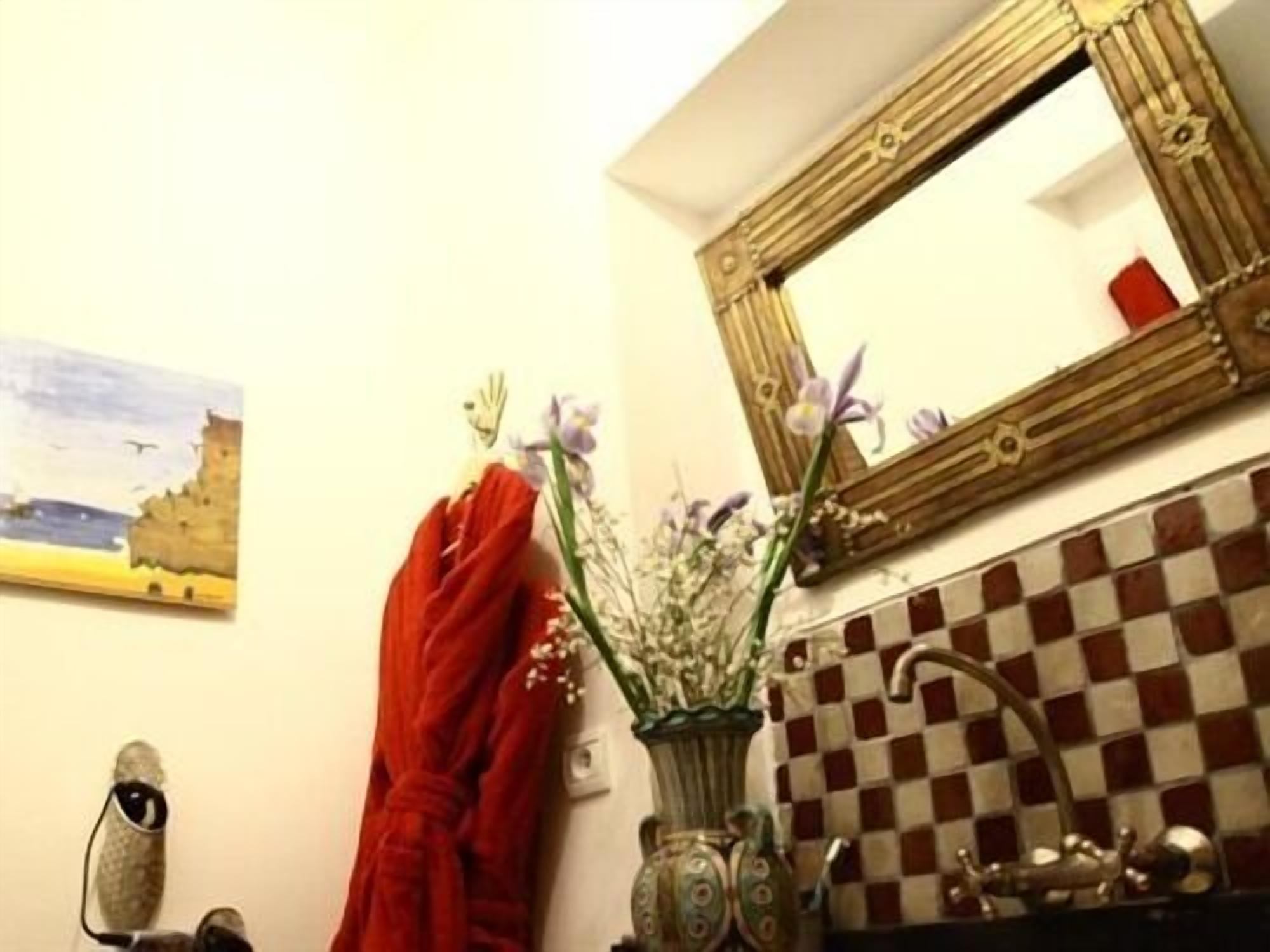 A bathroom with a checkered tile backsplash, a mirror with ornate framing, and a vase with flowers.