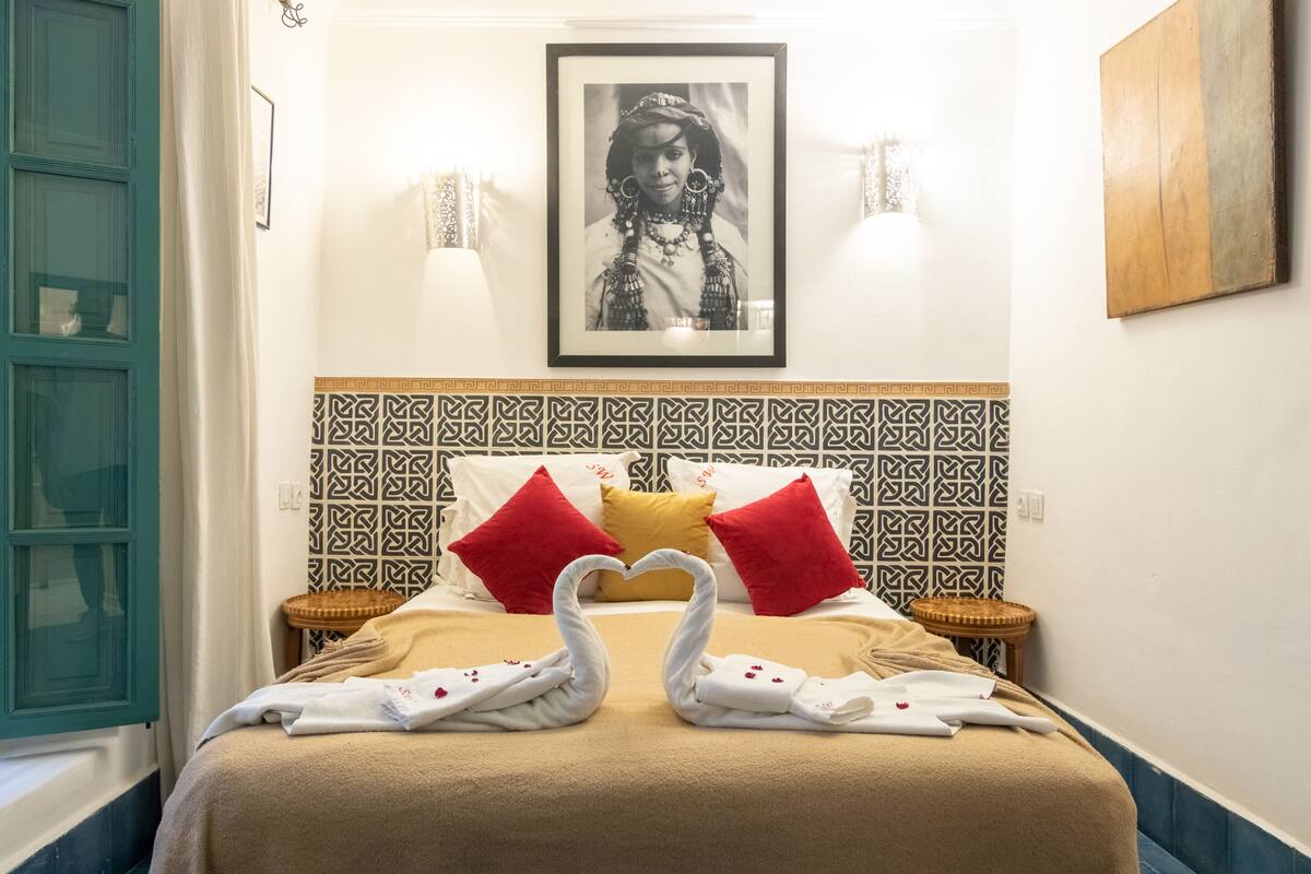Een hotelkamer met een bed, kussens, een lijst met een afbeelding en een muur met een decoratief patroon.