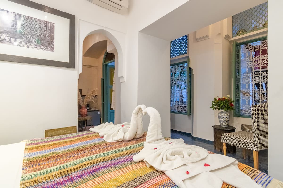 Een hotelkamer met een bed, een kleurrijk gestreept tapijt, een vaas met bloemen en een stoel.