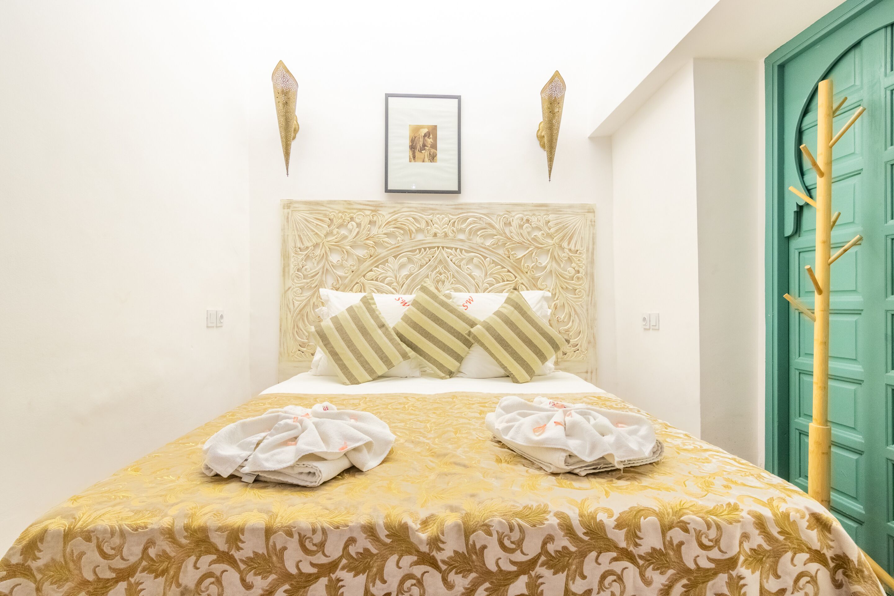 Una cama bien hecha con una colcha estampada, almohadas y un cuadro enmarcado encima.
