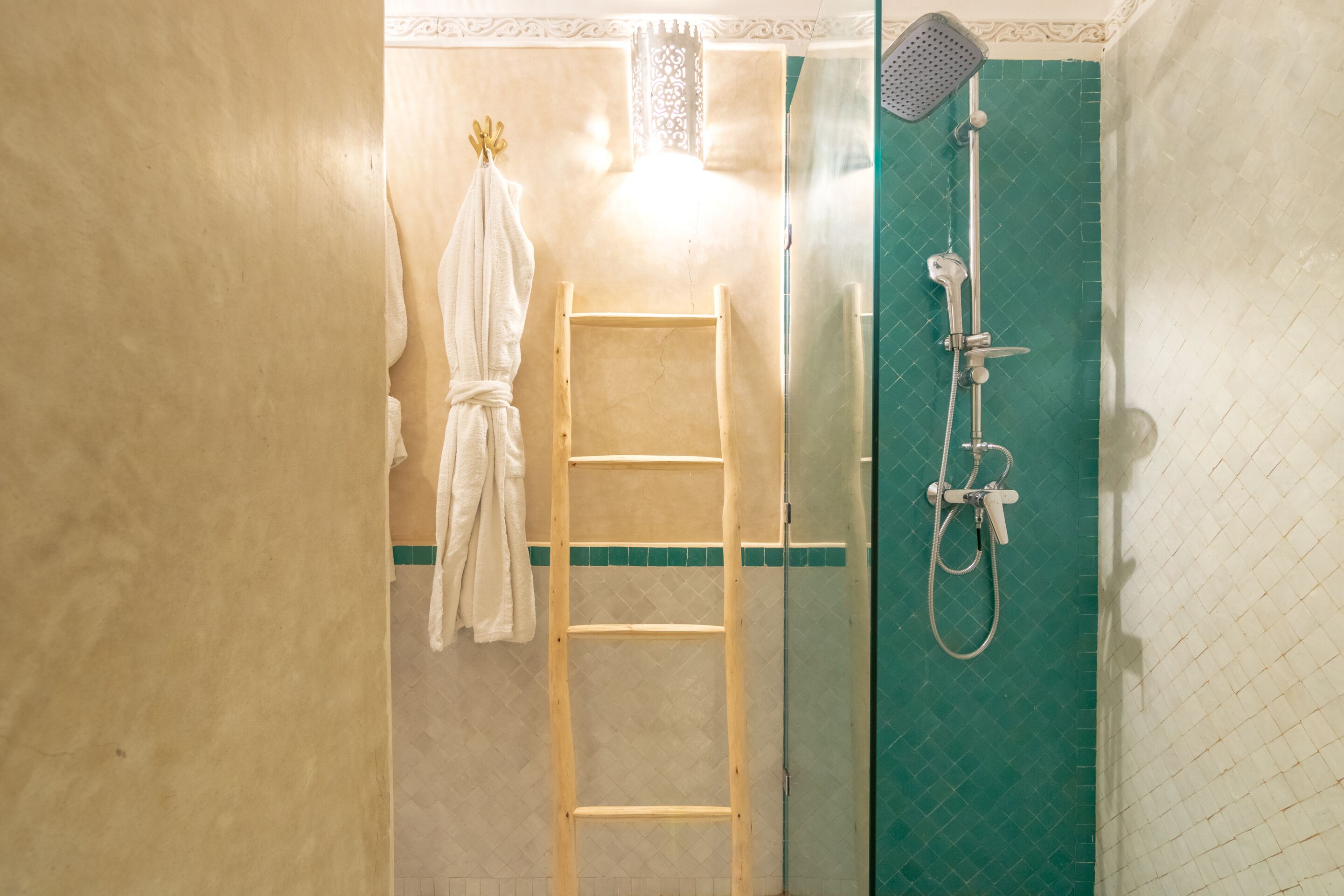 A bathroom with a shower, a wooden ladder, and a towel hanging on the wall.