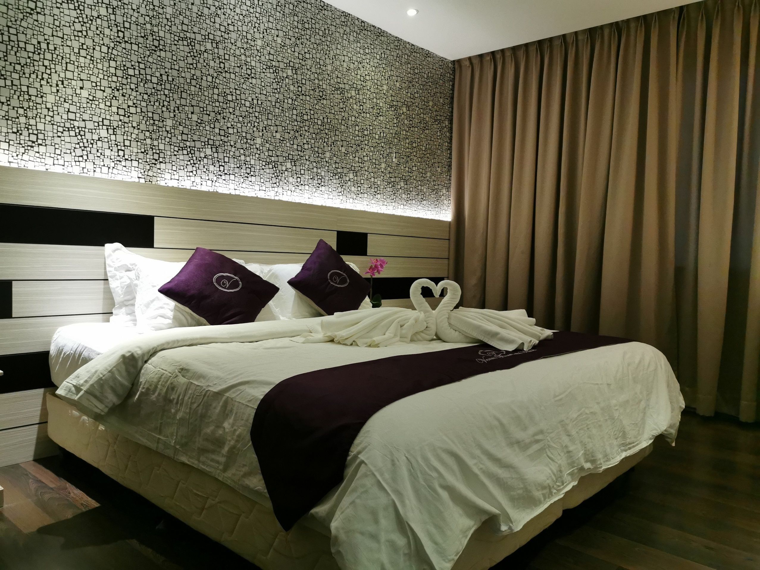 Une chambre d’hôtel avec un grand lit, une tête de lit ornée d’un motif en mosaïque et un rideau marron.