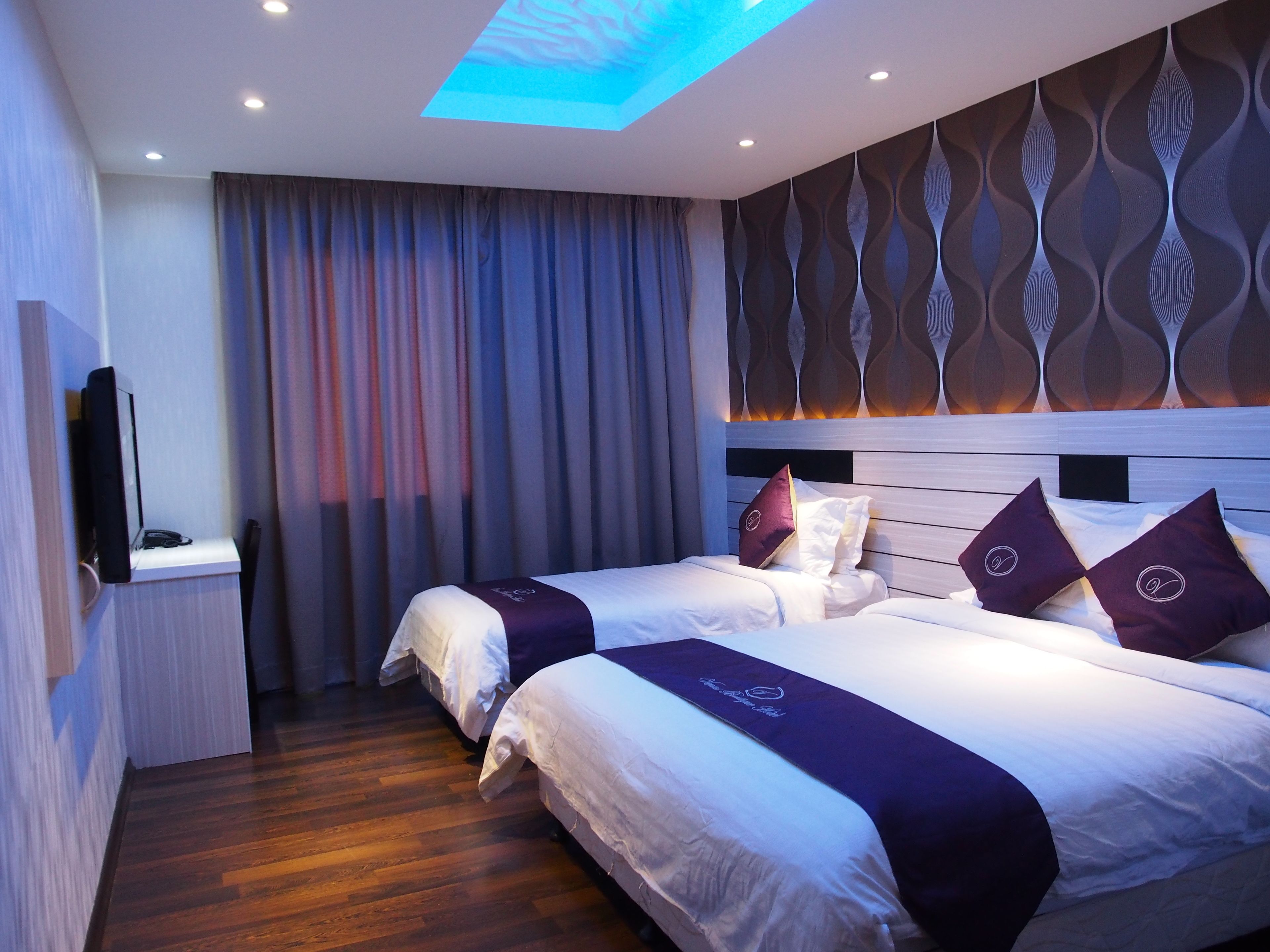A hotel room with two beds, a flat-screen TV, a wooden floor, and a patterned wall.