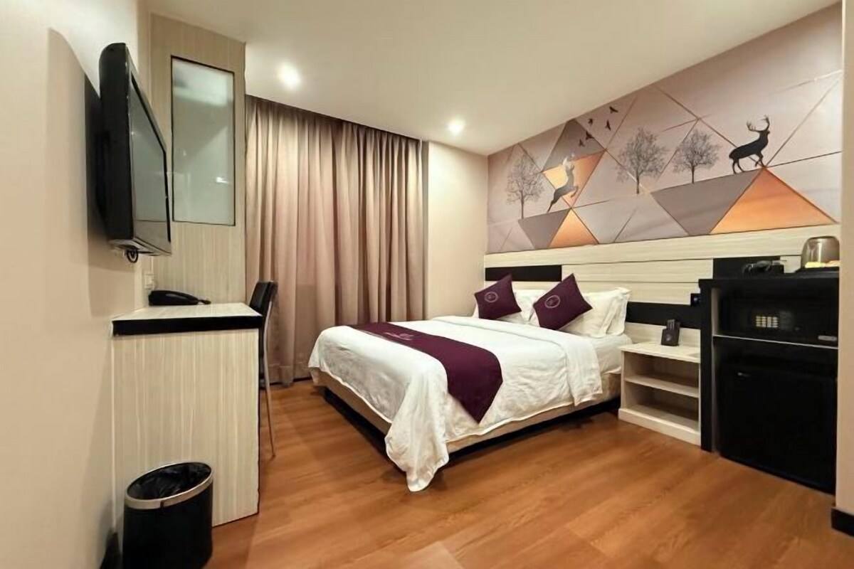 A hotel room with a bed, a desk, a TV, and a wall with a geometric design.