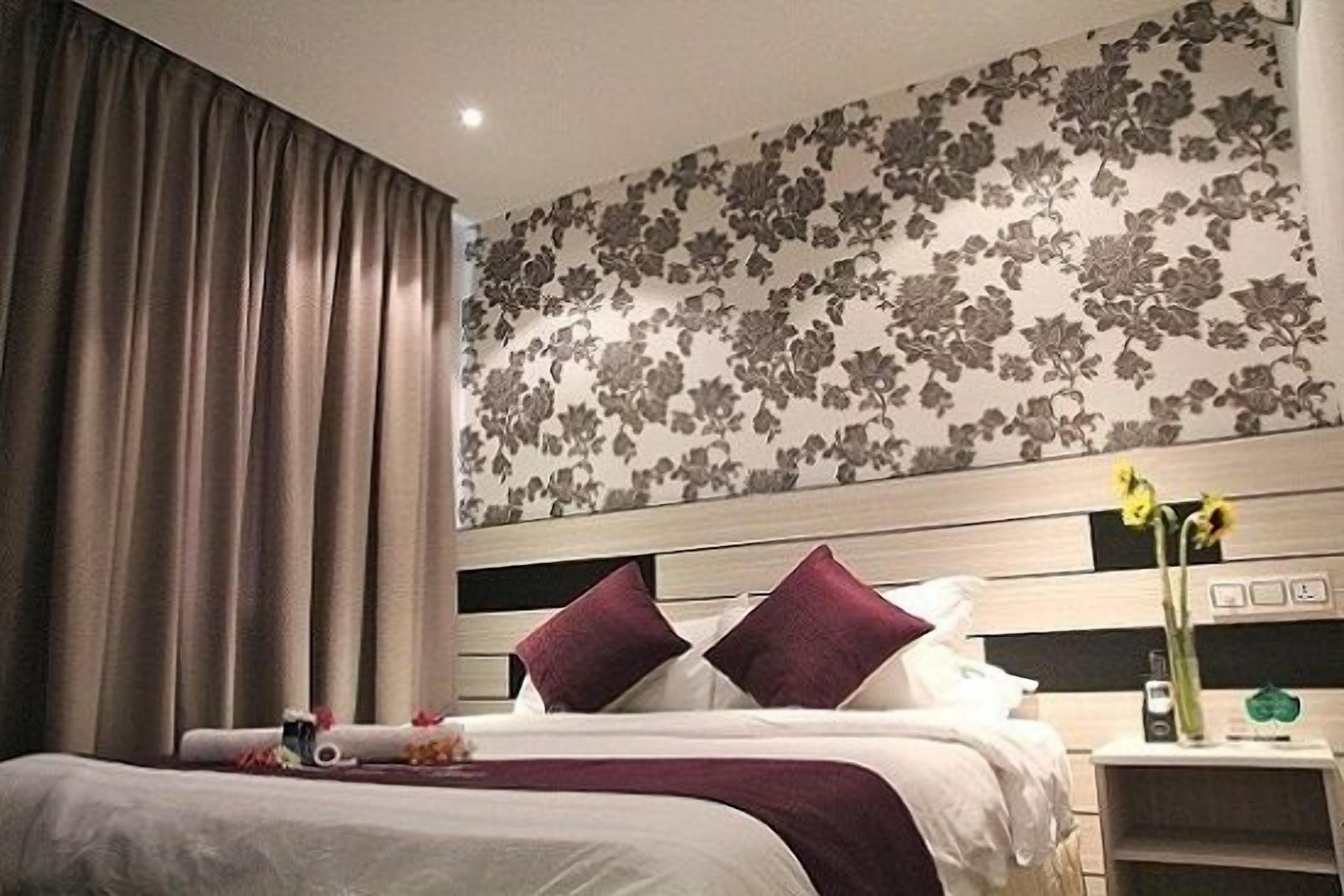 A hotel room with a bed, curtains, a nightstand, and a floral wallpaper.