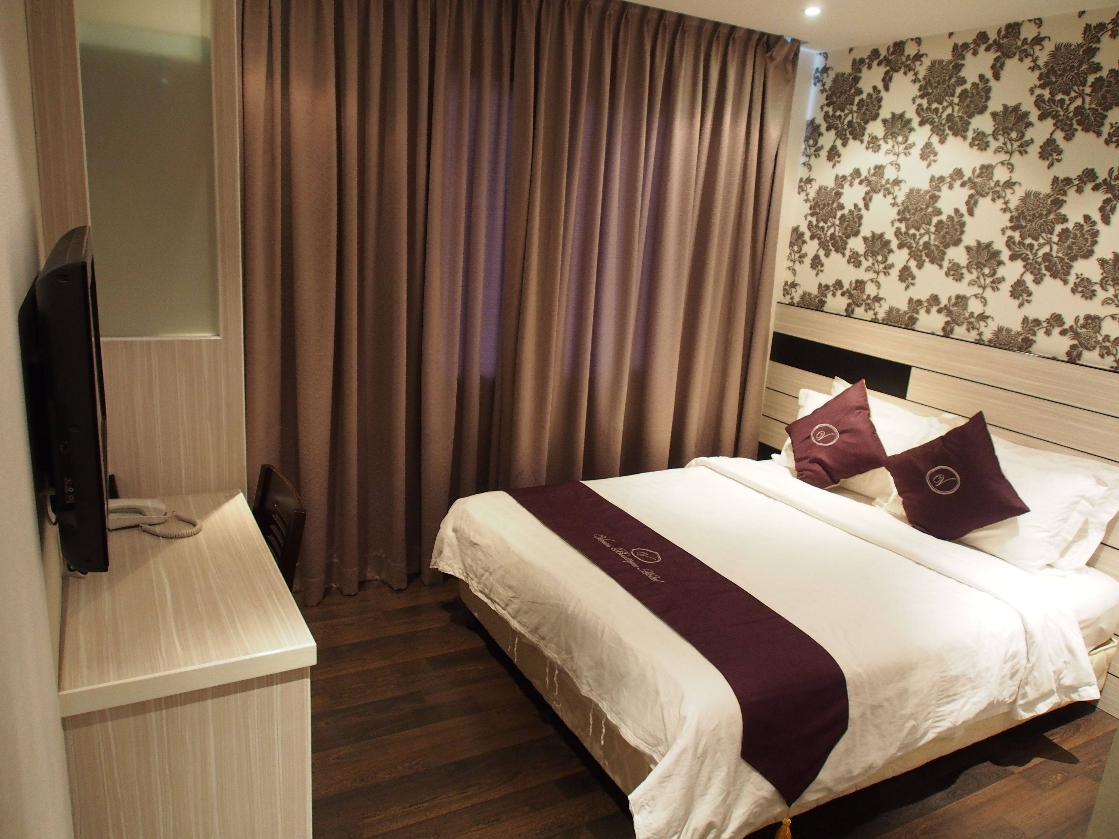 A hotel room with a bed, a TV, a telephone, and a curtain.