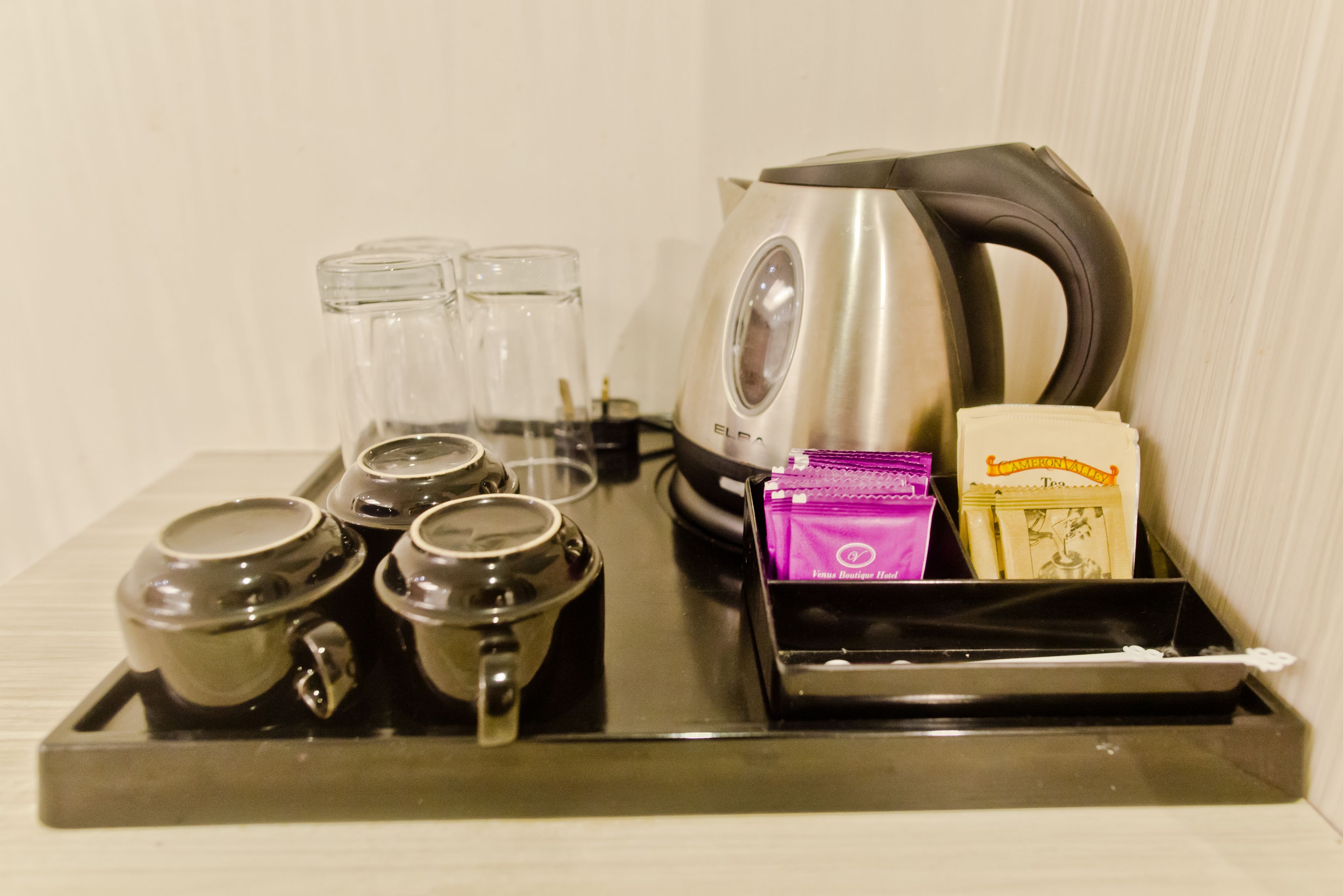 A tray with a kettle, four cups, and two small containers.