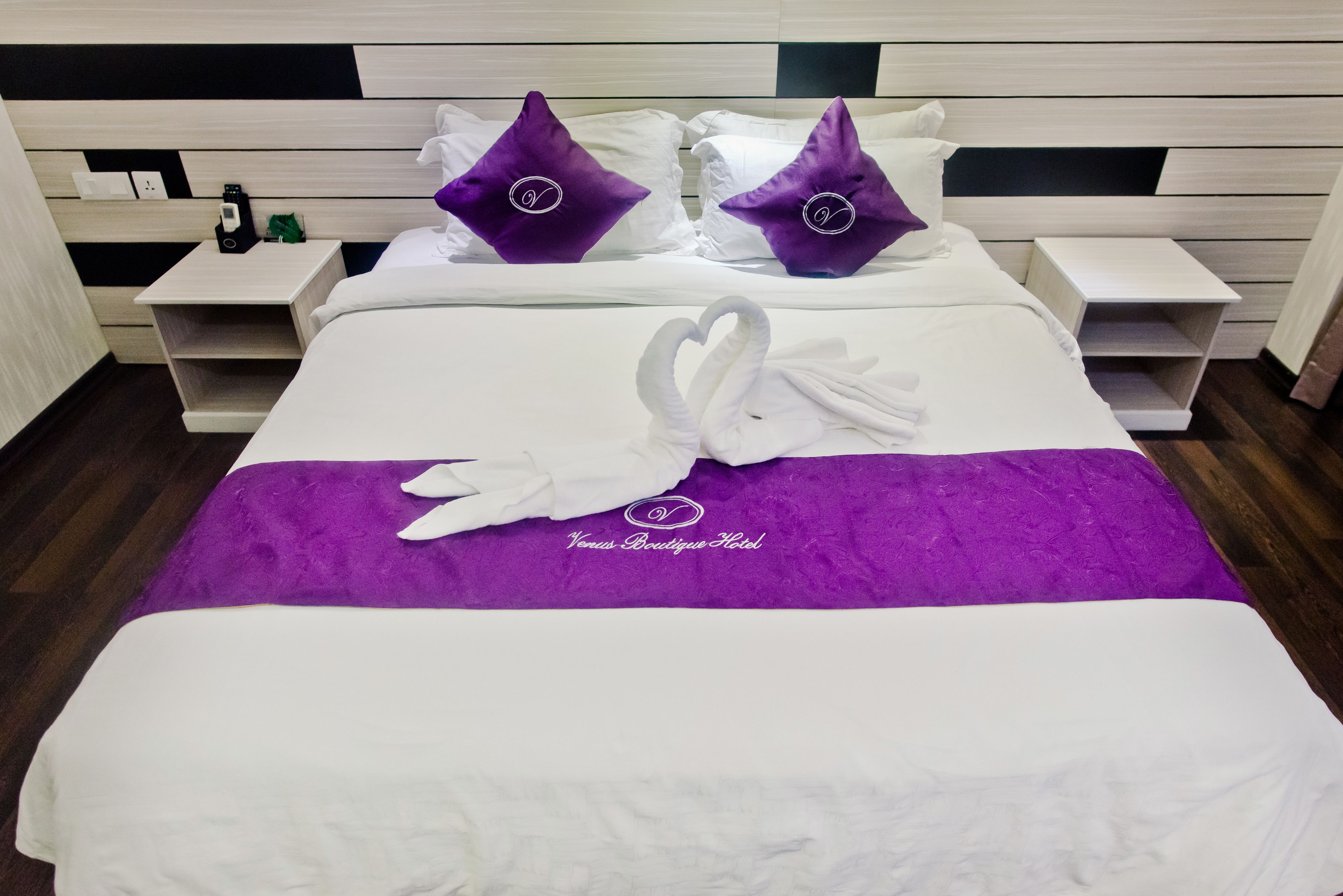 A hotel room with a bed, two nightstands, and a purple and white bedspread.