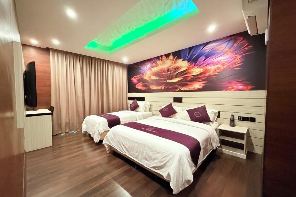 A hotel room with two beds, a flat-screen TV, a large floral mural, and a ceiling light fixture.