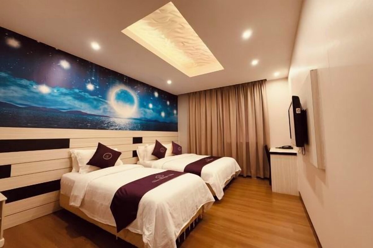 Habitación de hotel con dos camas, un mural del cielo nocturno, una lámpara en el techo y un televisor en la pared.