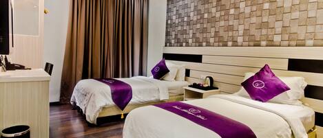 A hotel room with two beds, a wooden headboard, a wall-mounted TV, and a wooden floor.