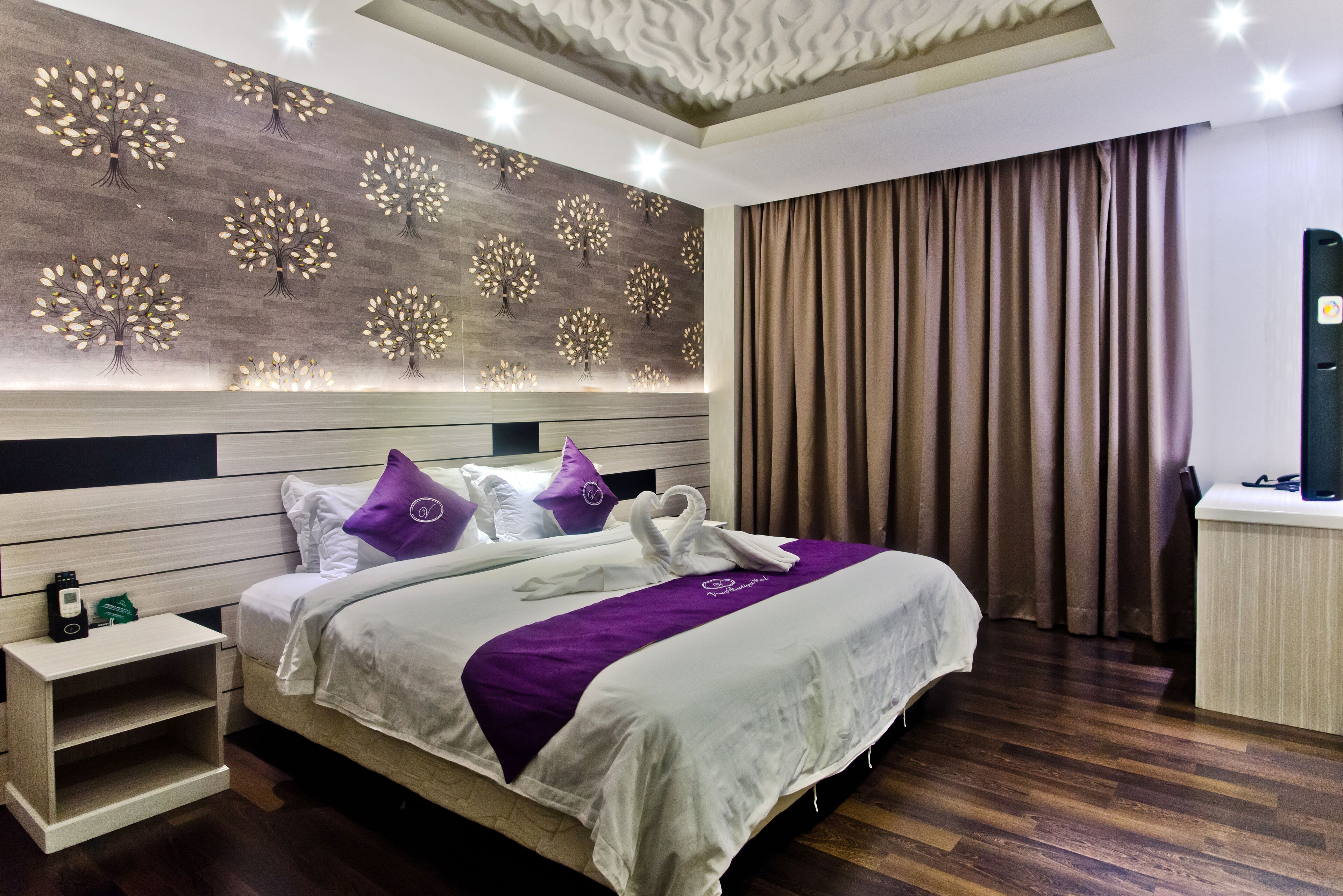 Une chambre d’hôtel avec un grand lit, une table de chevet, un mur décoré de motifs d’arbres et un rideau.