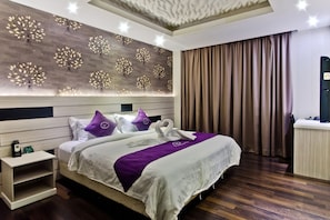 A hotel room with a large bed, a nightstand, a wall with tree designs, and a curtain.