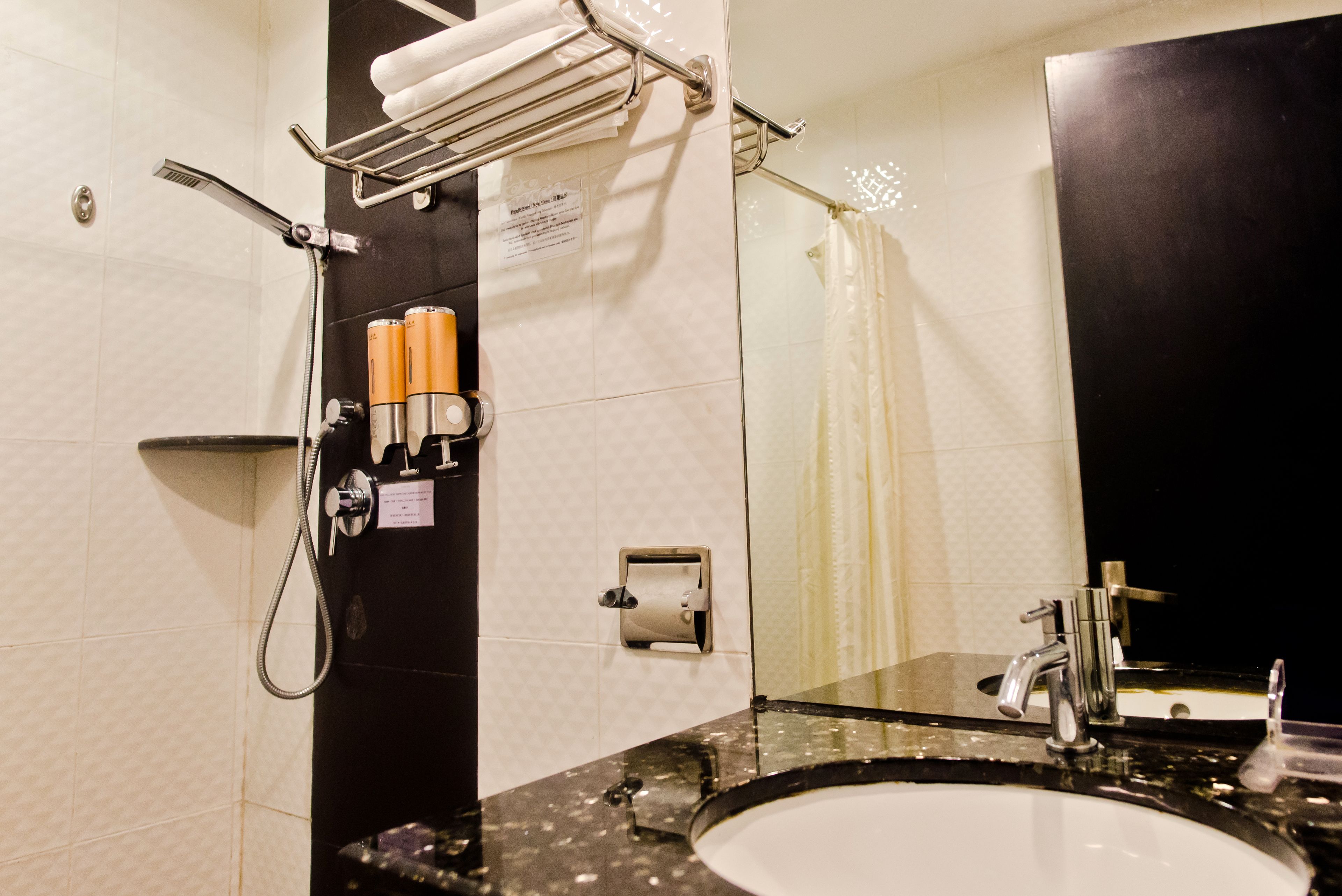 Un baño con lavamanos, espejo, toallero, cabezal de ducha y artículos de aseo.