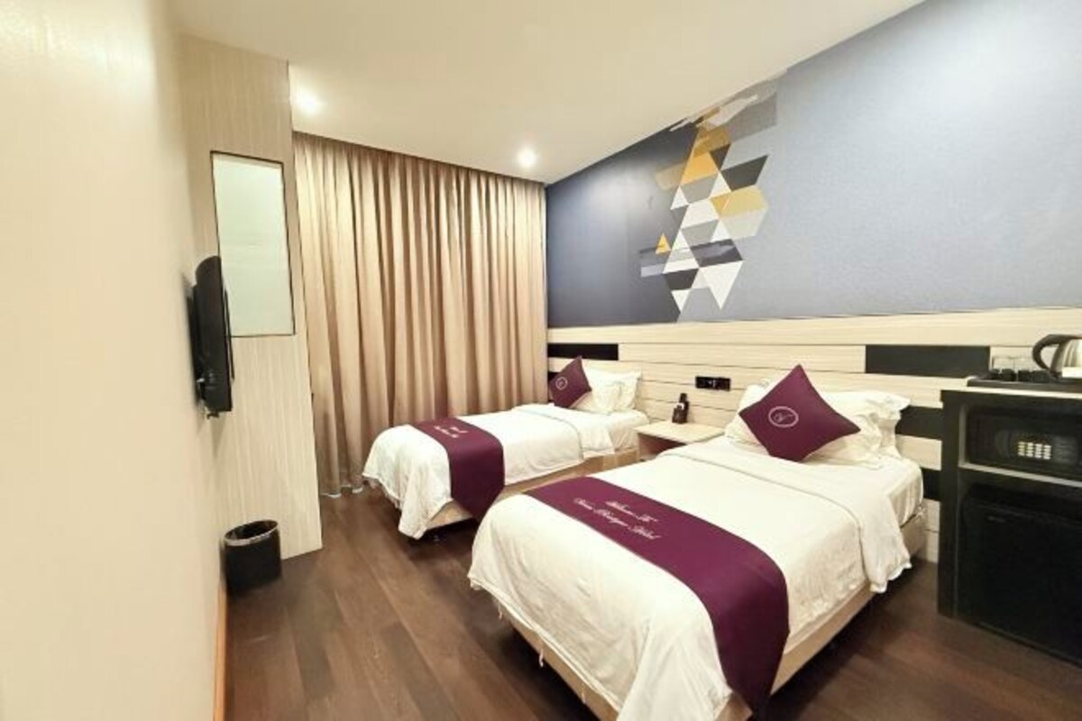 A hotel room with two beds, a TV, a desk, and a wall with geometric artwork.