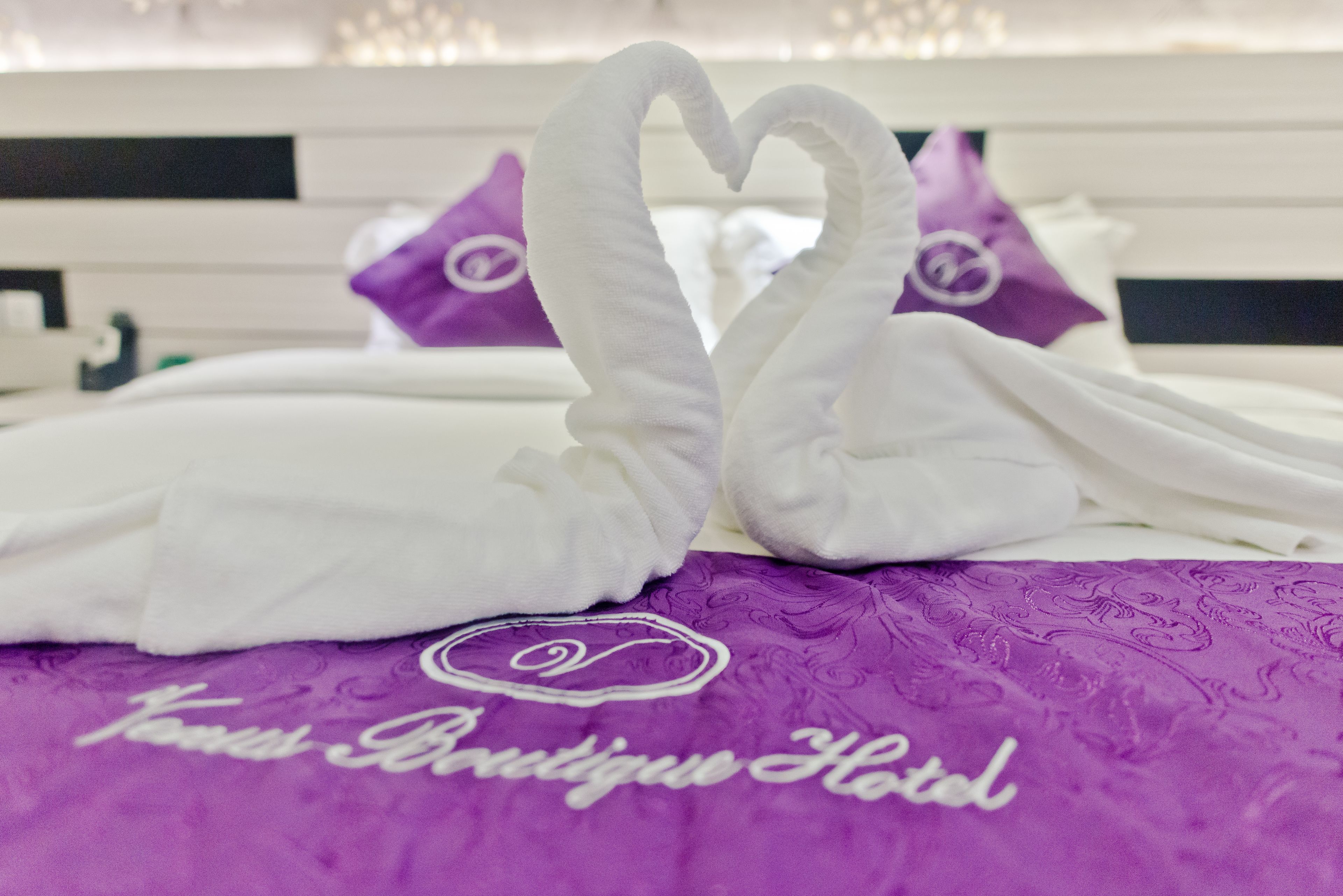 A bed with white pillows and a purple blanket with the text "Yours Boutique Hotel".