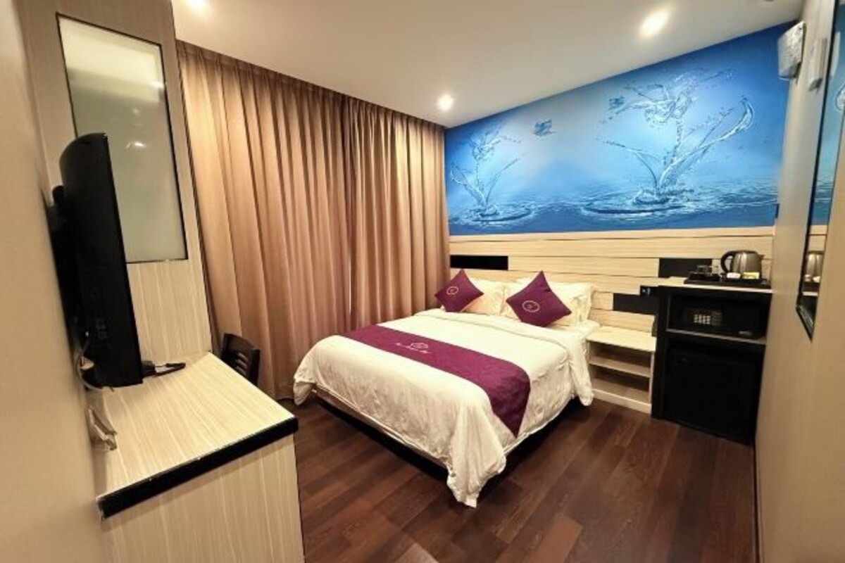 A hotel room with a bed, a desk, a television, and a painting on the wall.