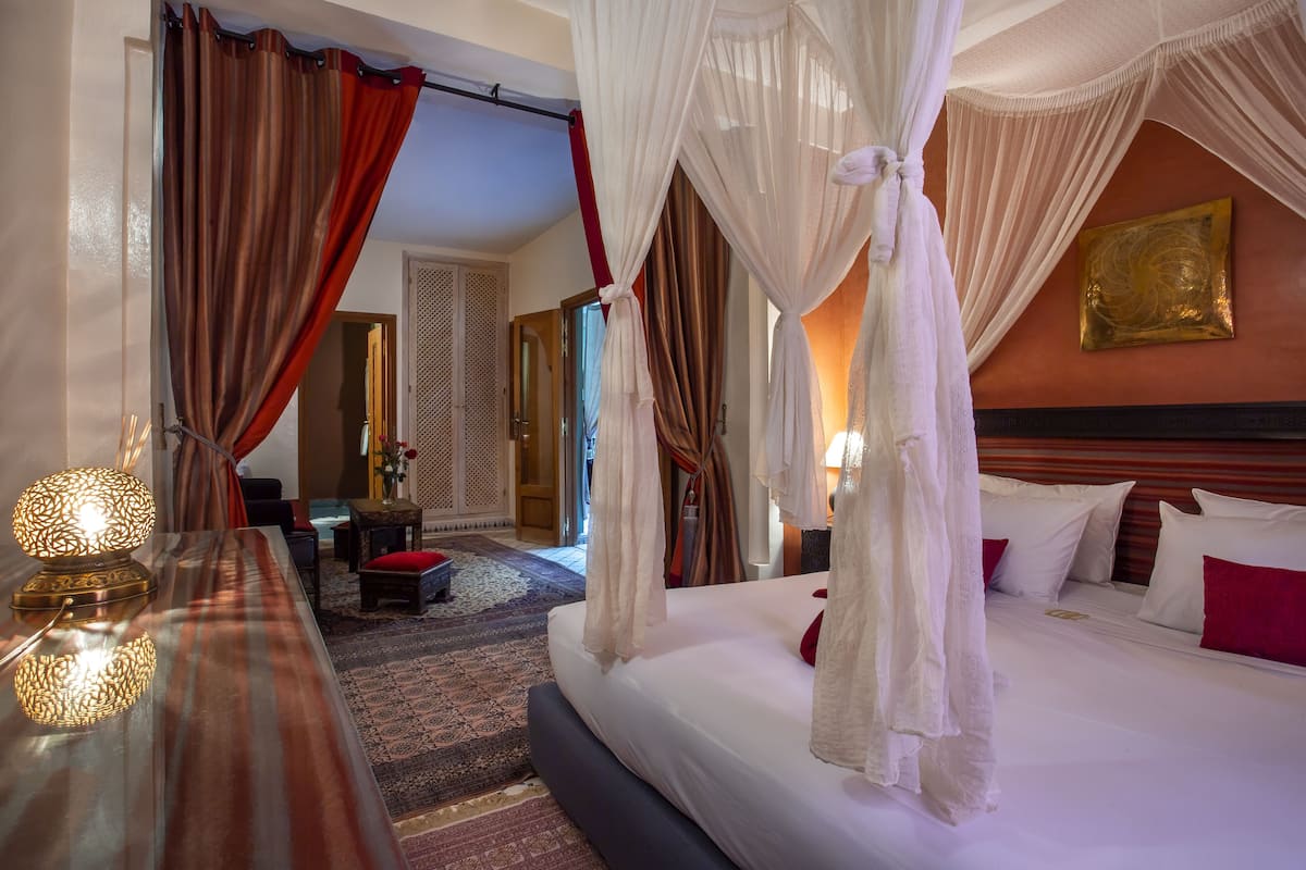 A hotel room with a bed, a nightstand, a lamp, and a view of the hallway.