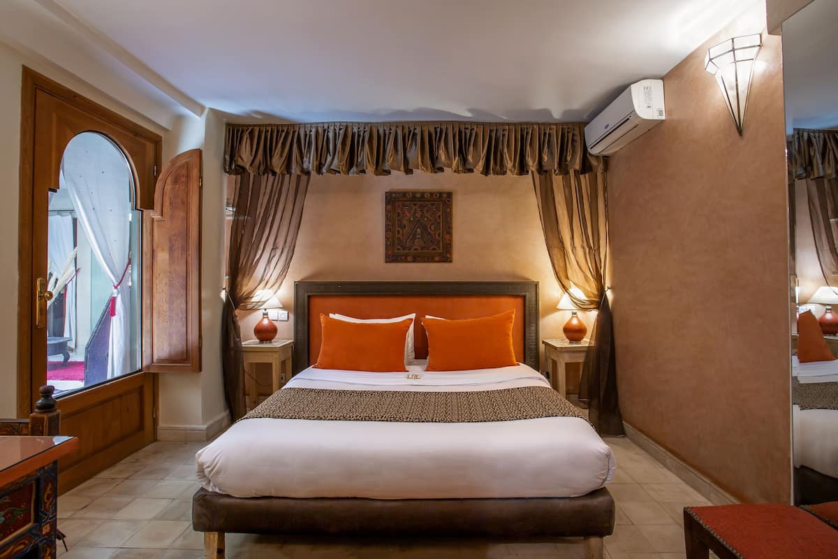A neatly arranged hotel room with a large bed, two bedside tables, a mirror, and a wall-mounted air conditioner.