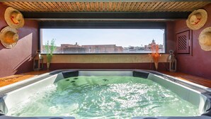 Un jacuzzi con panel de control, rodeado de sombreros de paja, una ventana con vistas a edificios y un jarrón con plantas.