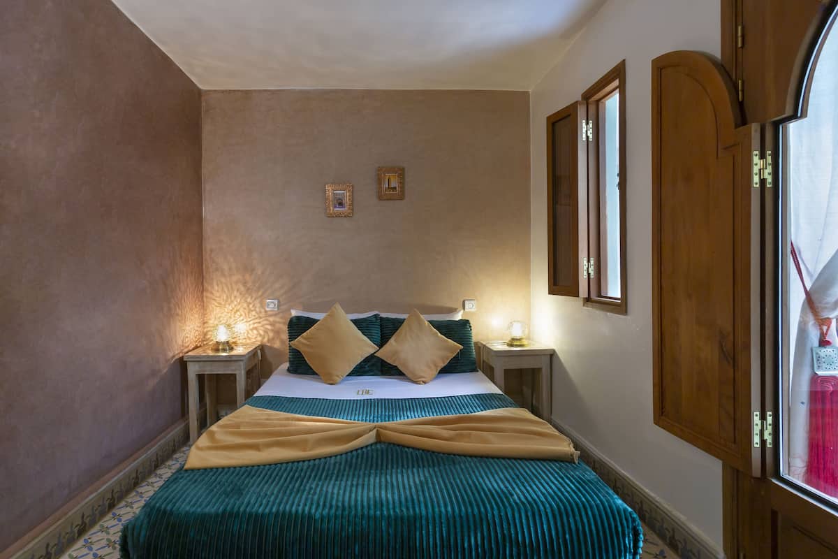 A neatly made bed with a striped bedspread and two pillows, a bedside table with a lamp, and a wooden wardrobe with a mirror.