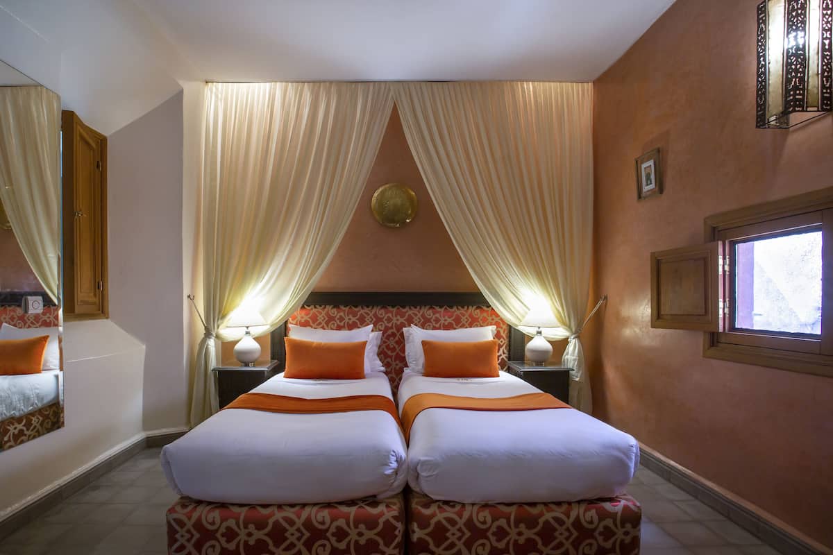 A hotel room with two beds, a large mirror, and a window with curtains.