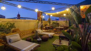 Terraza en la azotea con sillones de descanso, mesas y luces colgantes con forma de estrella.