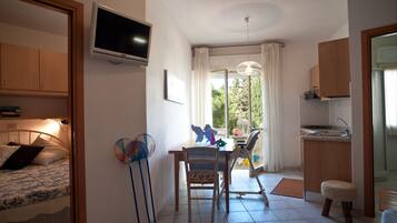 Una habitación compacta con cama, escritorio, silla, televisor y una pequeña kitchenette.