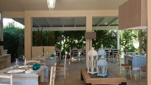 Un espace de restauration en plein air avec des tables pour deux personnes, des chaises blanches et des lanternes.