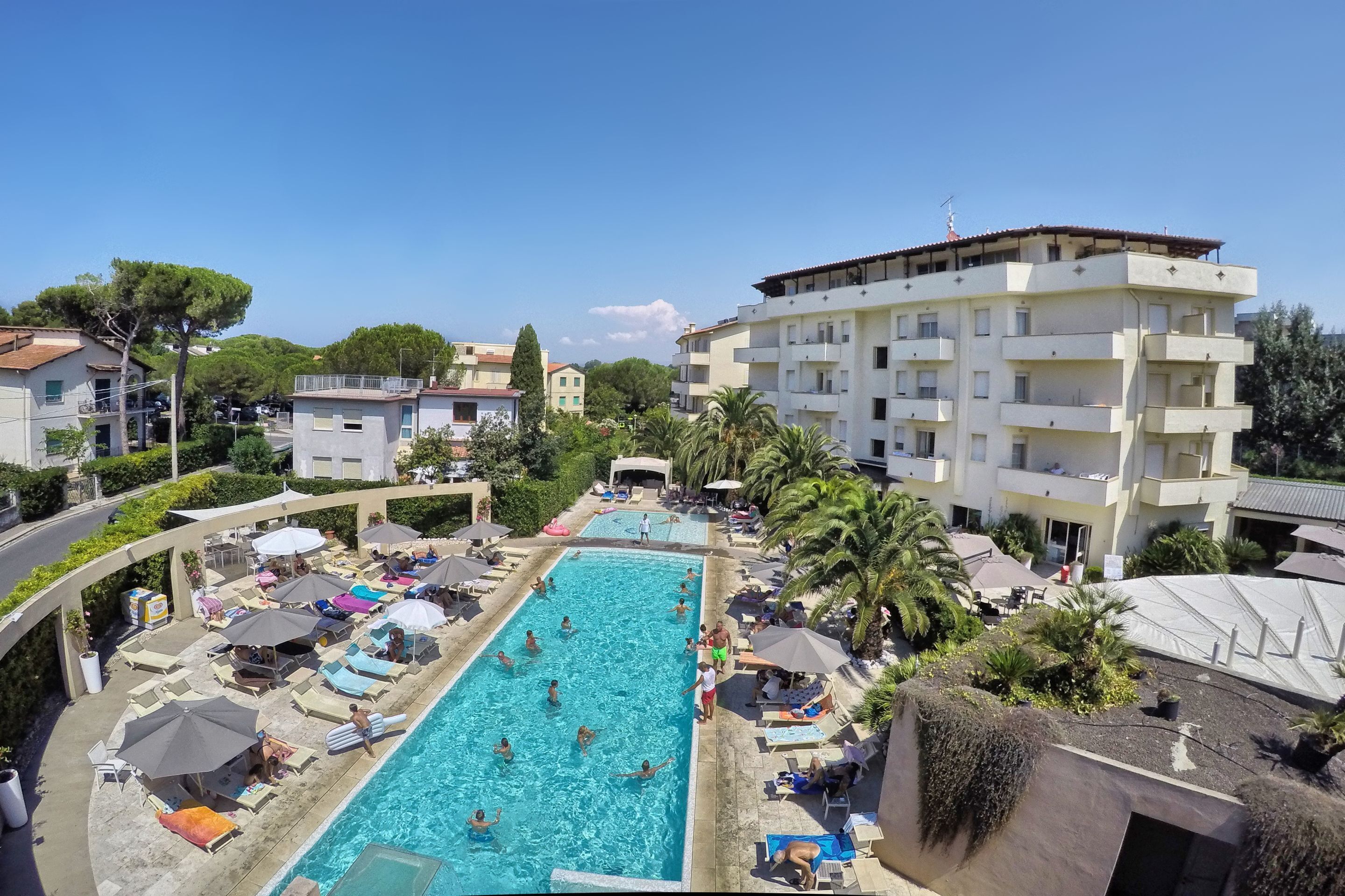 A swimming pool area with lounge chairs and umbrellas, surrounded by buildings and greenery.