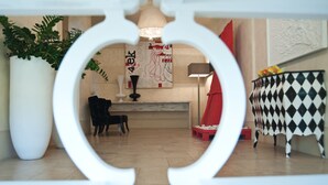 Un intérieur moderne avec un cadre décoratif blanc, une plante en pot, une chaise noire, une chaise rouge, une table à motifs noir et blanc, et un mur orné d’un motif abstrait rouge et blanc.