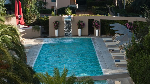 Une piscine rectangulaire agrémentée d’une cascade, entourée de chaises longues et de plantes en pot.