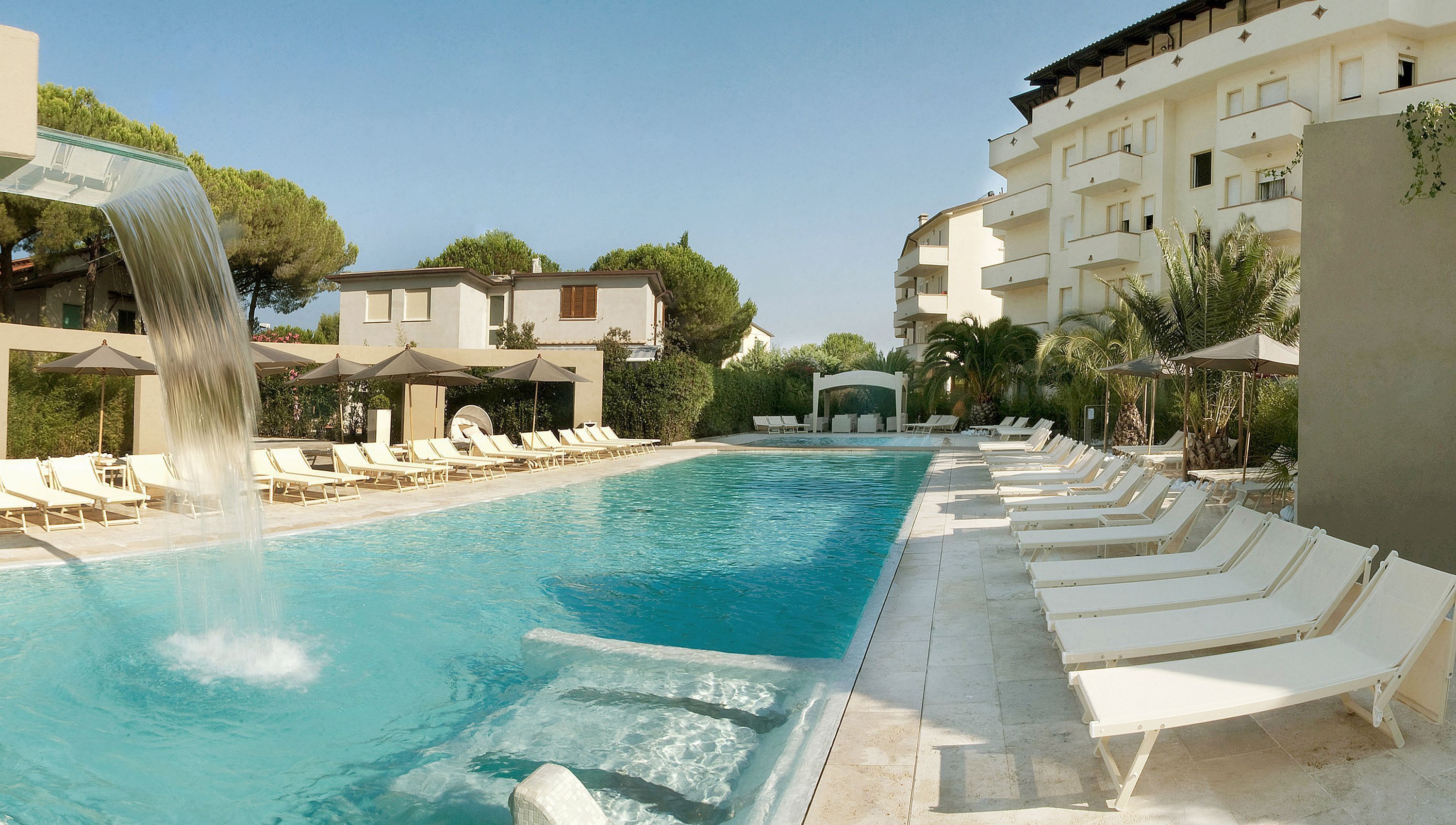 A swimming pool with a waterfall feature, surrounded by lounge chairs and umbrellas.