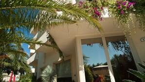 Un bâtiment moderne avec une entrée en verre, entouré d’une végétation luxuriante et de fleurs aux couleurs vives.