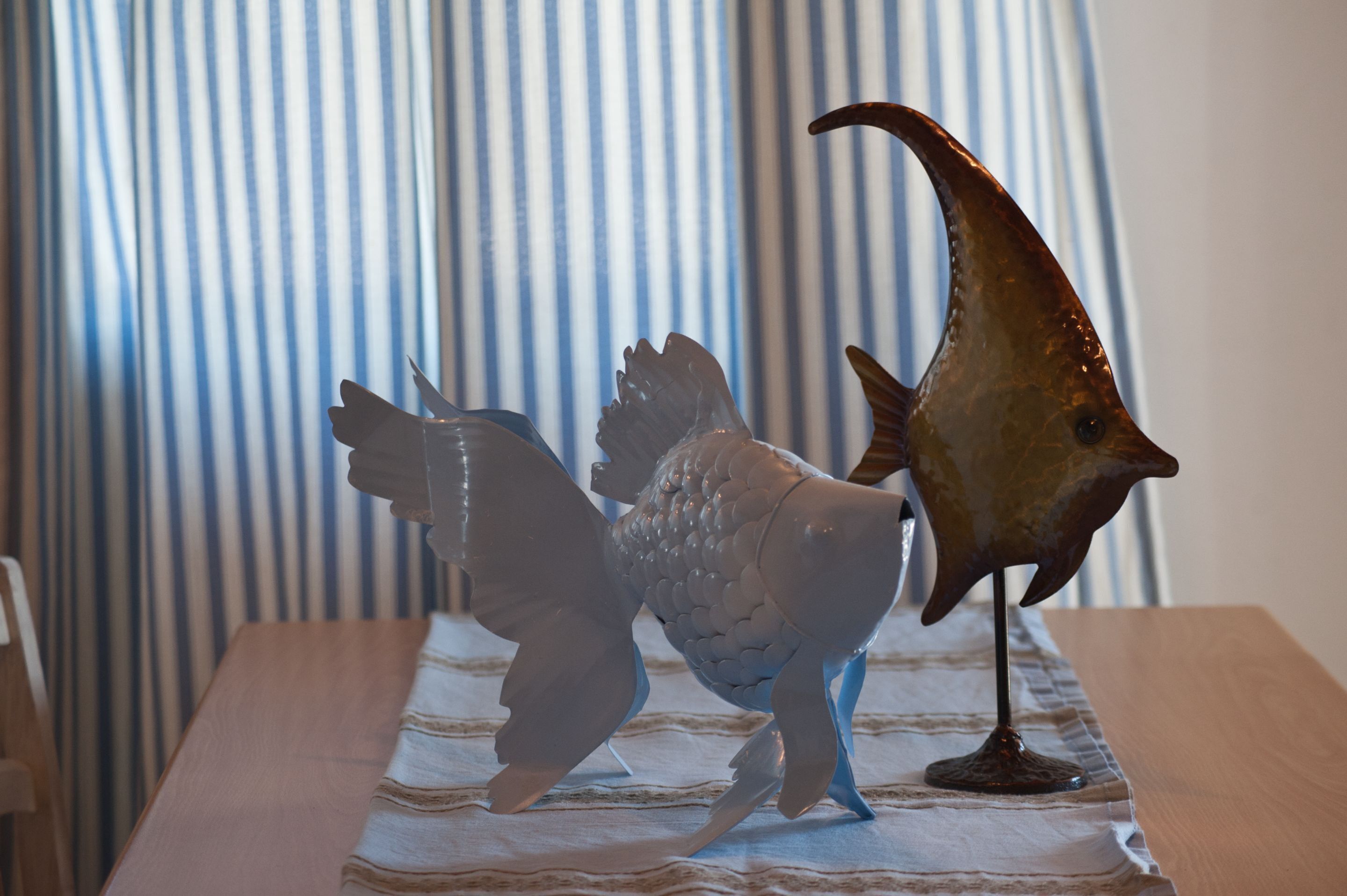 Una mesa con una escultura decorativa de pez y una cortina a rayas al fondo.
