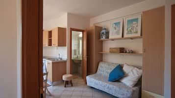 Un espacio habitable compacto con kitchenette, un sofá con cojines y un taburete pequeño.