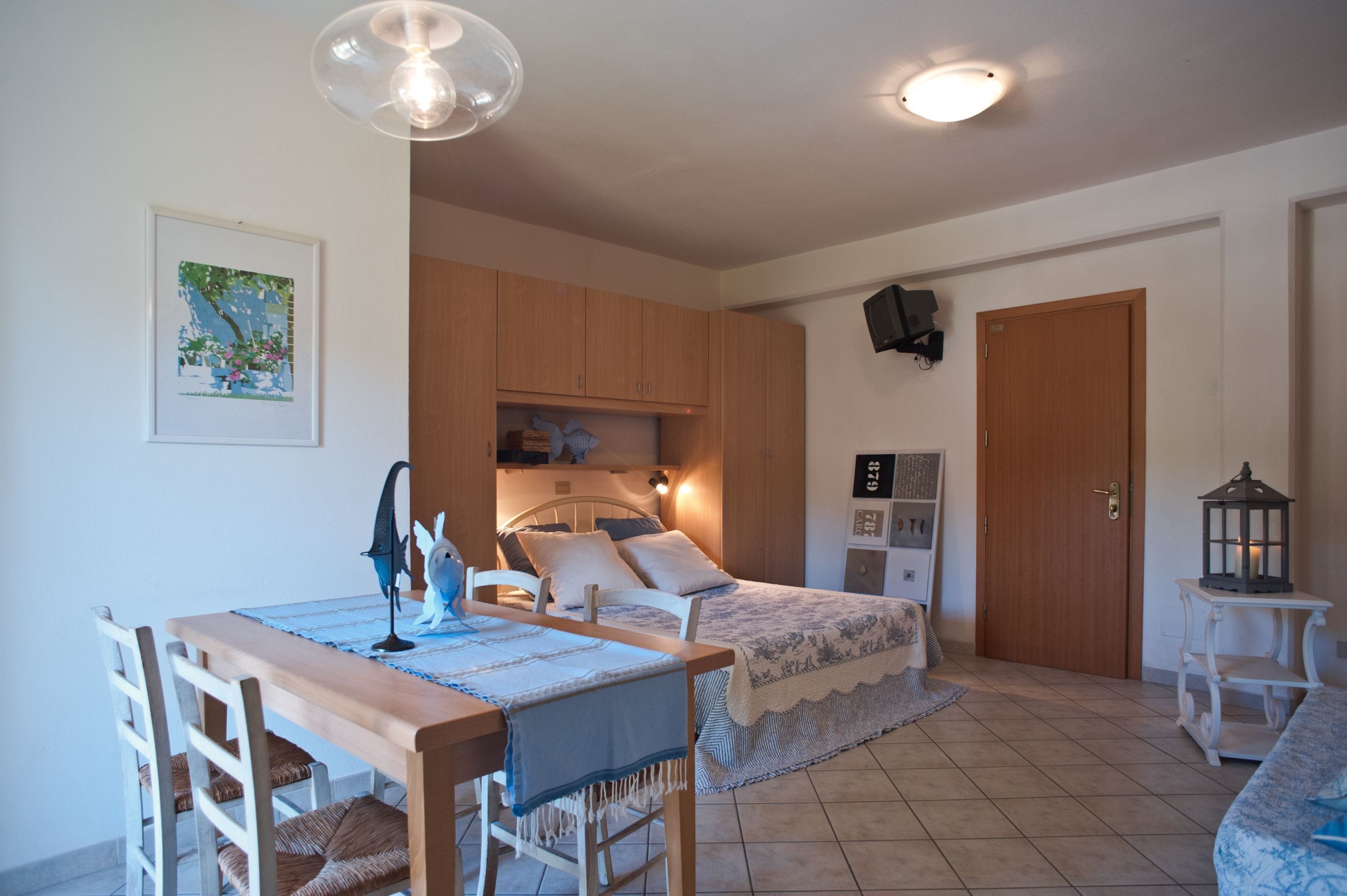 A bedroom with a bed, bedside table, lamp, and a small table with chairs.
